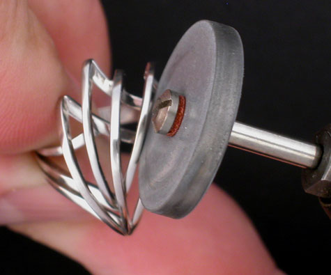 Close-up view of a jeweler using an abrasive wheel to prefinish a platinum ring that incorporates flat wires as part of the design