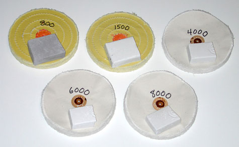 Two yellow-treated wheels labeled “800” and “1500,” and three white wheels labeled “4000,” “6000,” and “8000,”indicating the abrasive grades of  the platinum polishing compounds placed on top of the wheels, 