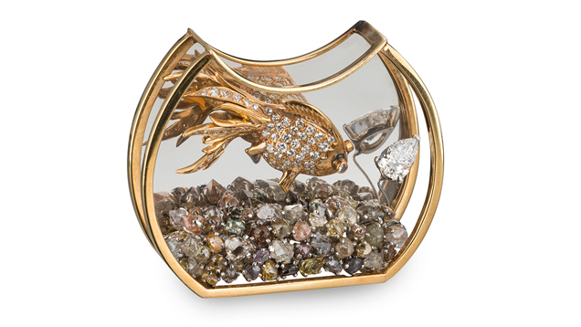 A crescent-shaped bowl with a flat bottom trimmed in gold holds rough diamond gravel and a gold and diamond fish.