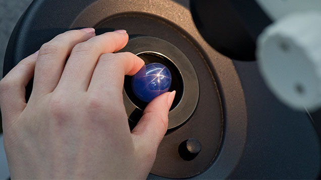 Hand holding starry night sapphire under a microscope. 