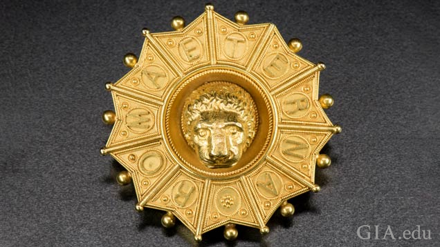 Gold pendant features a lion head in the middle; the frame around it is separated into sections with each section displaying a letter that taken together spell out ROMA ETERNA.
