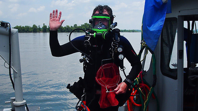 ボートで淡水産貝を持ちながら手を振るダイバー