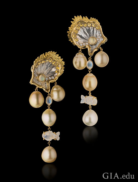 ホワイト サファイアとイエロー サファイア、そして18Kイエロー ゴールドをアクセントにして貝殻をかたどったマザー オブ パールからぶら下がる南洋真珠。イヤリングの上部からは、魚の形をしたものも含むムーンストーンのアクセントも吊り下げられている。