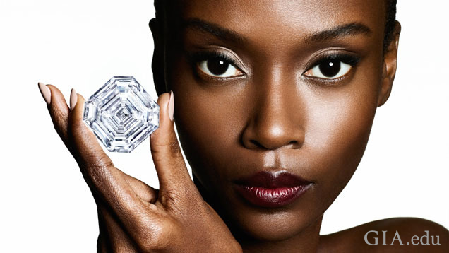 モデルが3本の指で大きな隅切りスクエアのダイヤモンドを持っている。