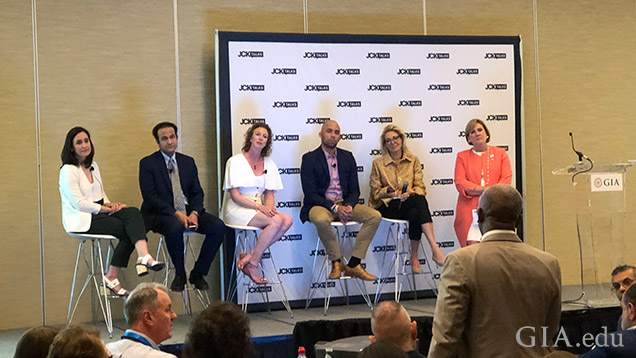 聴衆の前のステージで椅子に座っている6人。