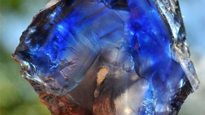 割れたサファイア結晶の平たい破片（約20カラット）は、鮮やかな青色に白い微粒子の帯が交ざっており、中心部は「チョコレート」ブラウンのシルクで満たされている。