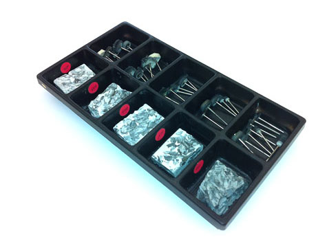 Tray containing five compartments of platinum polishing compound in various grits, along with five adjacent compartments containing attachments for working with the compound at the bench