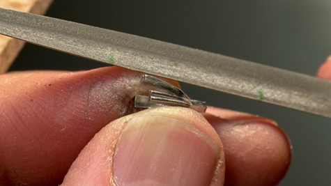 Jeweler using a small abrasive tool to prefinish a platinum ring’s peg setting for a solitaire ring