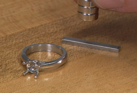 Solitaire ring setting without gemstone sitting next to a sizing wire with magnets above the wire