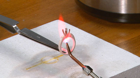 Photograph of a platinum peg setting being soldered to a yellow gold mounting using a torch