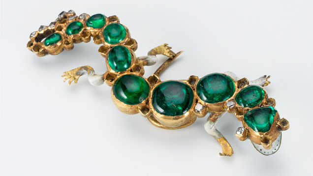 这枚金镶祖母绿帽饰形似一条蝾螈，是 Cheapside Hoard 最具代表性的作品之一。 前方的搪瓷看似张开的嘴巴，其中甚至有类似牙齿的黑色斑点。 别针上装饰着产自哥伦比亚的凸圆面祖母绿，而尾部则镶嵌着桌形切工钻石。