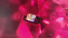 A crystal inclusion in red spinel shown in darkfield illumination (left) and fiber-optic lighting (right). Photomicrographs by Isabelle Corvin; field of view 1.78 mm.