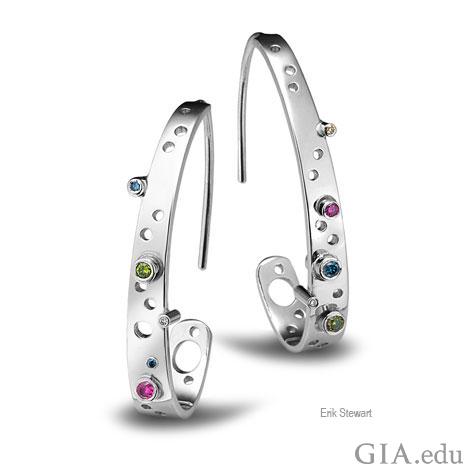 Front view of platinum “J” hoop earrings designed by Erik Stewart, featuring a variety of small, bezel-set colored stones and circles of different sizes that use negative space as a design motif. 